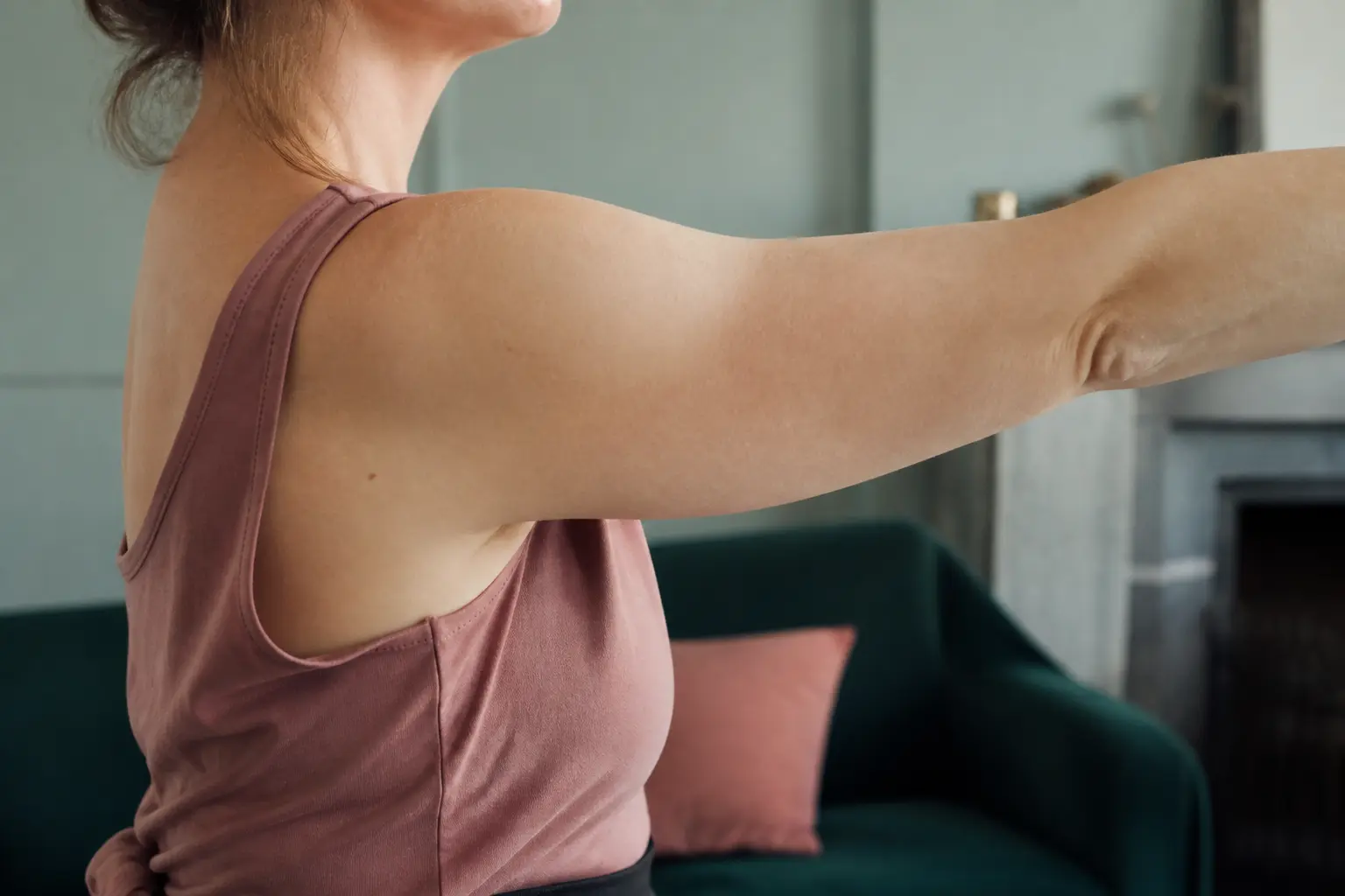 Personne levant un bras dans un salon, épaule craque sans douleur, lumière douce et fond flou.