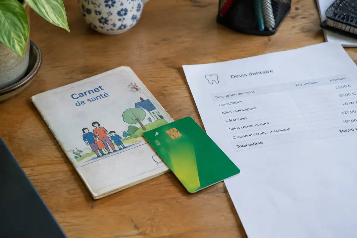 Carnet de santé avec une carte Vitale posée à côté d'un devis dentaire