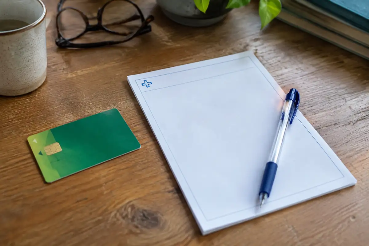 Carte vitale et bloc d'ordonnance vierge avec un stylo posés sur un bureau en bois